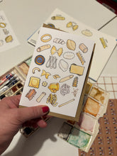 Hand holding a card with pasta illustrations on a surface with other cards and stationery items.